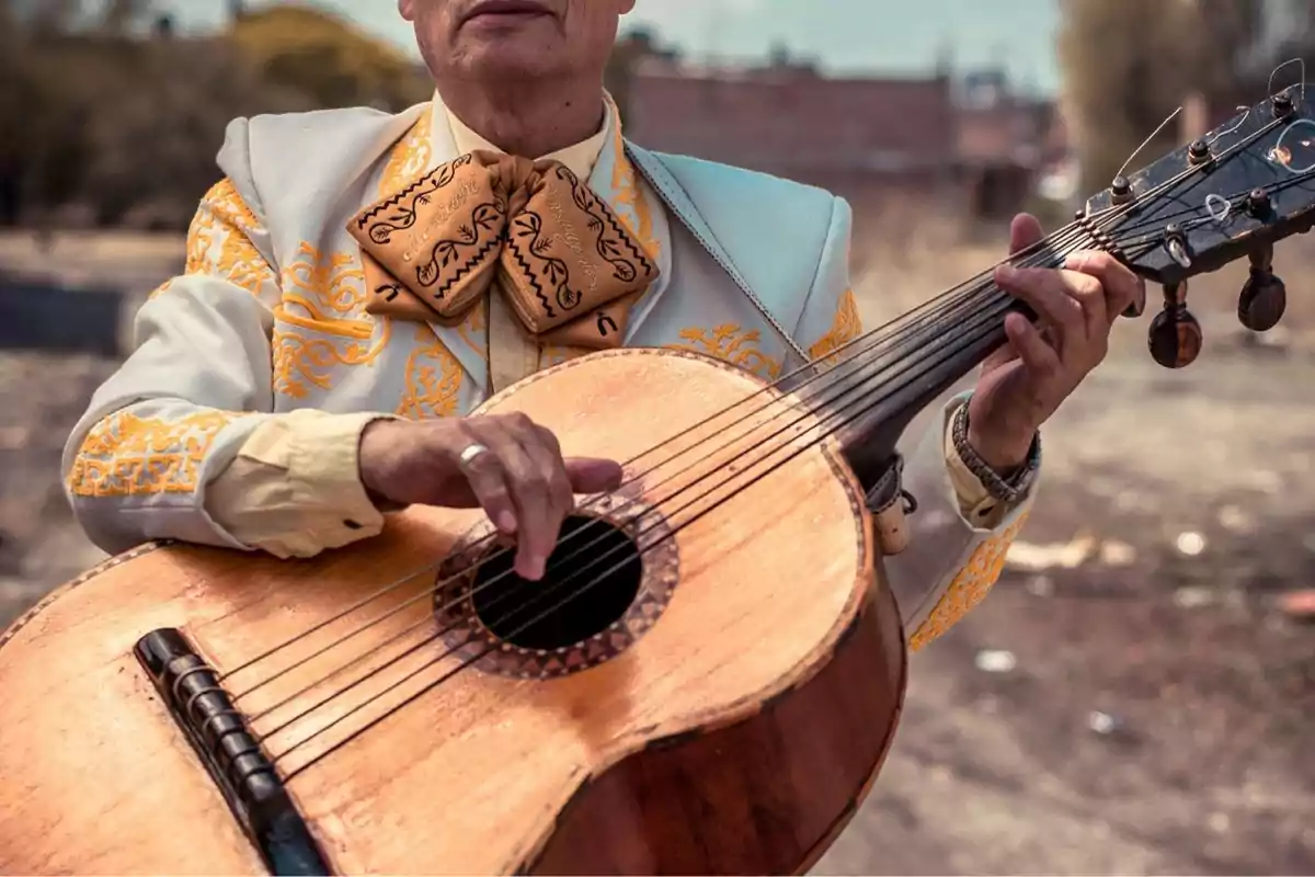 Un hombre vestido con un traje tradicional de mariachi toca una guitarra en un entorno al aire libre.