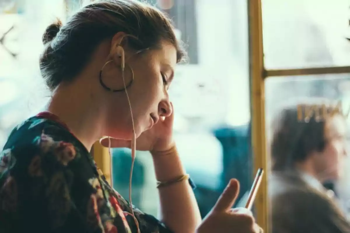 Persona con auriculares mirando su teléfono móvil en un café.