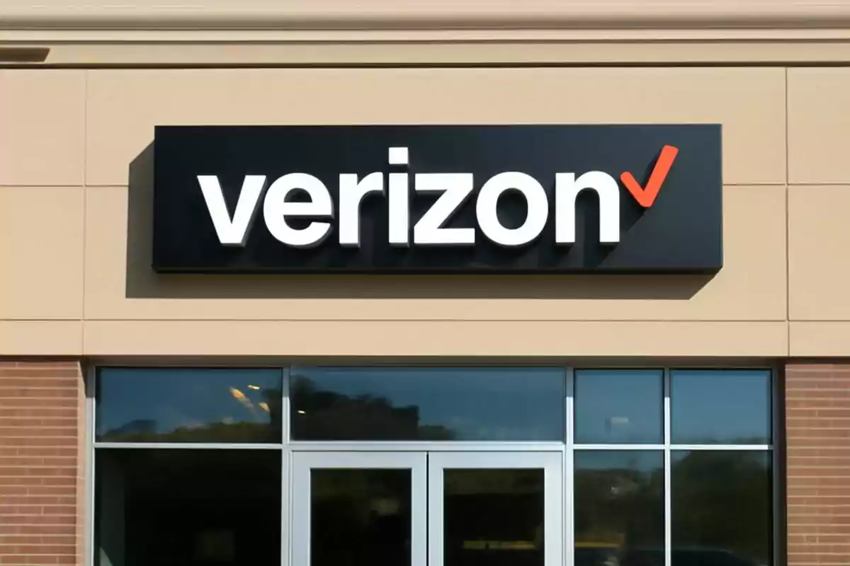 Fachada de una tienda con el logotipo de Verizon en un cartel negro sobre una pared de ladrillo y paneles beige.