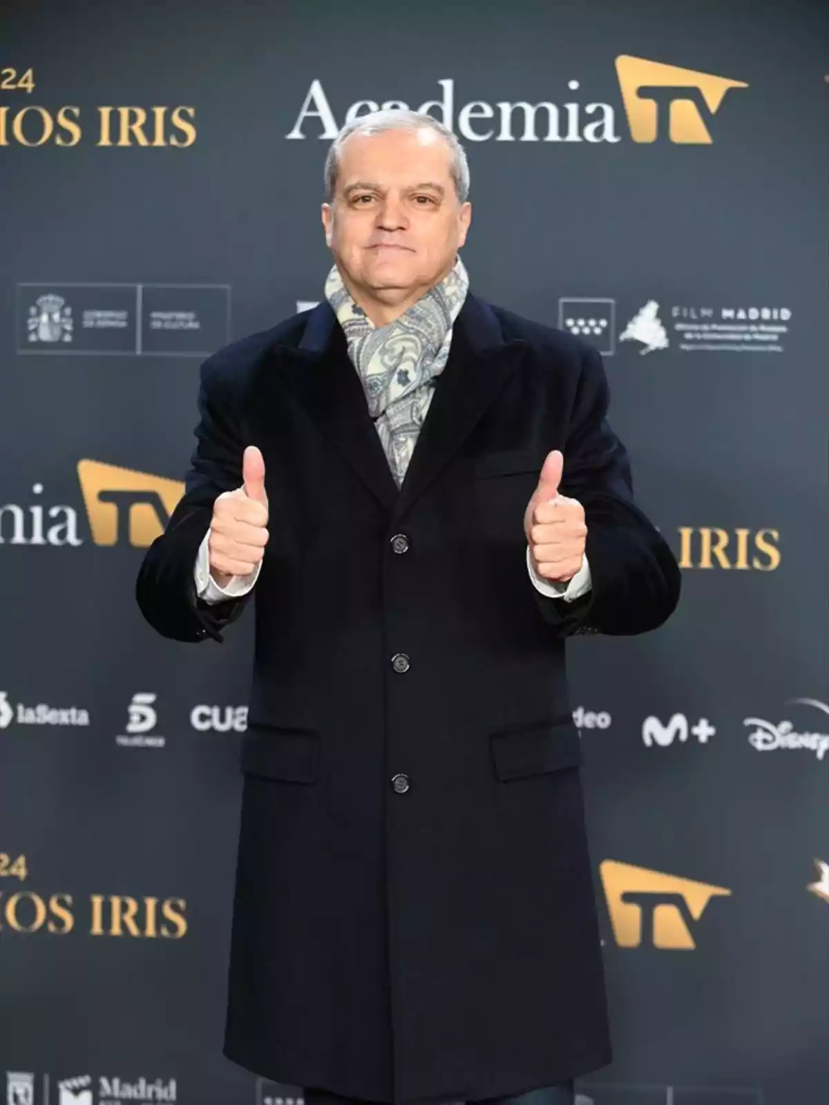 Ramón García con abrigo oscuro y bufanda posando con los pulgares hacia arriba frente a un fondo de la Academia de Televisión. Ramón García con abrigo oscuro y bufanda posando con los pulgares hacia arriba frente a un fondo de la Academia de Televisión.