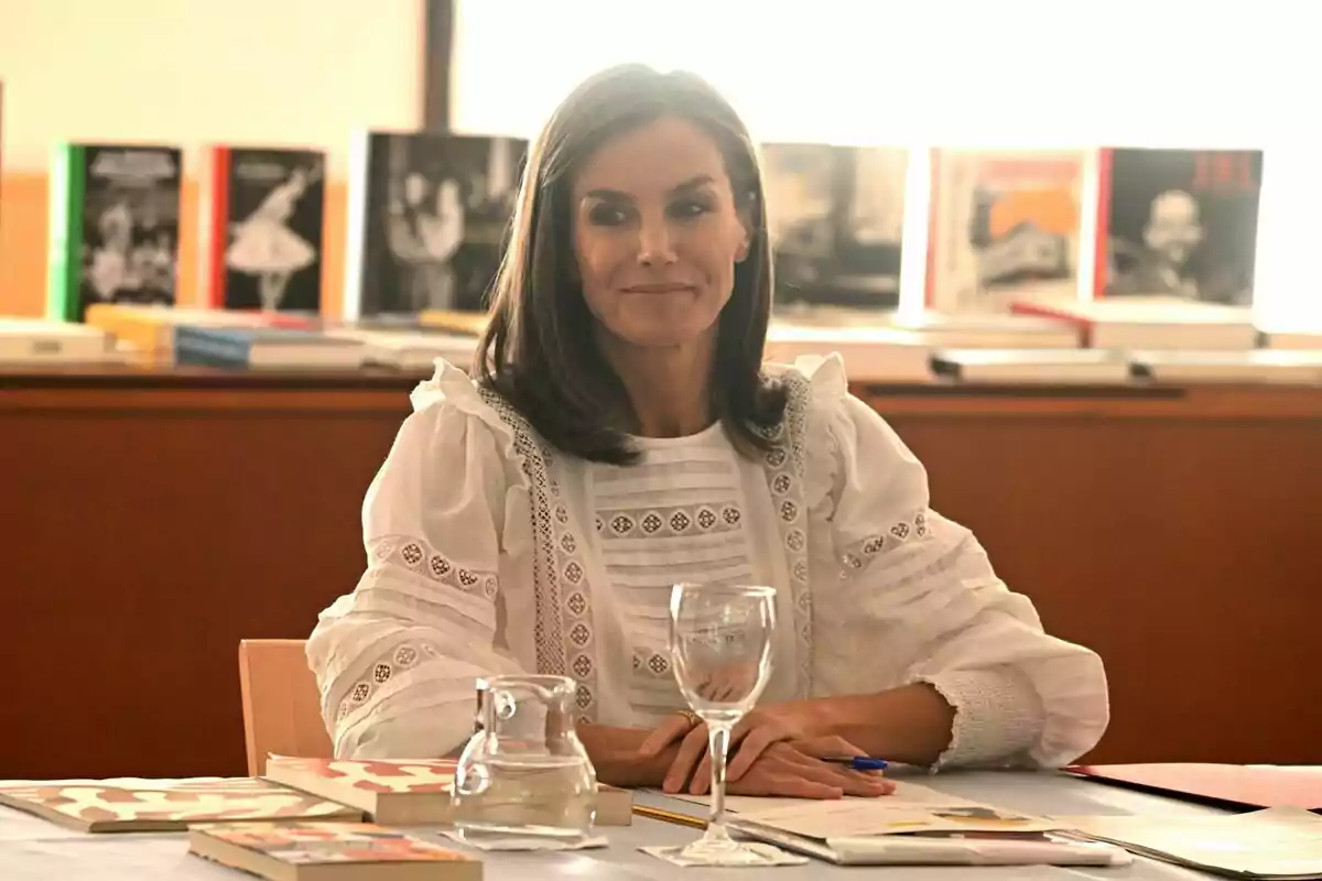 Letizia sonriendo mirando a un lado con una blusa blanca y las manos encima de la mesa con un bolígrafo en la mano Letizia sonriendo mirando a un lado con una blusa blanca y las manos encima de la mesa con un bolígrafo en la mano