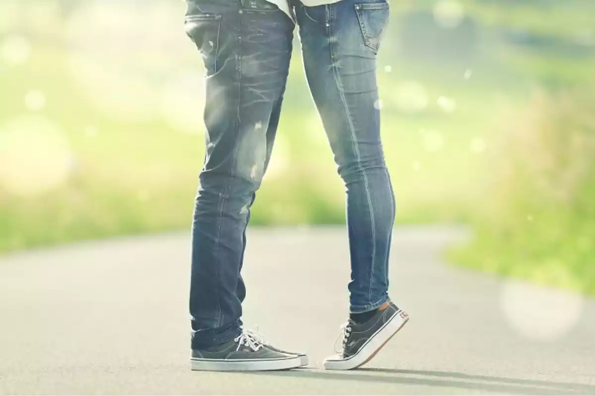 Pareja de pie en un camino, ambos usando jeans y zapatillas, con un fondo desenfocado de naturaleza.